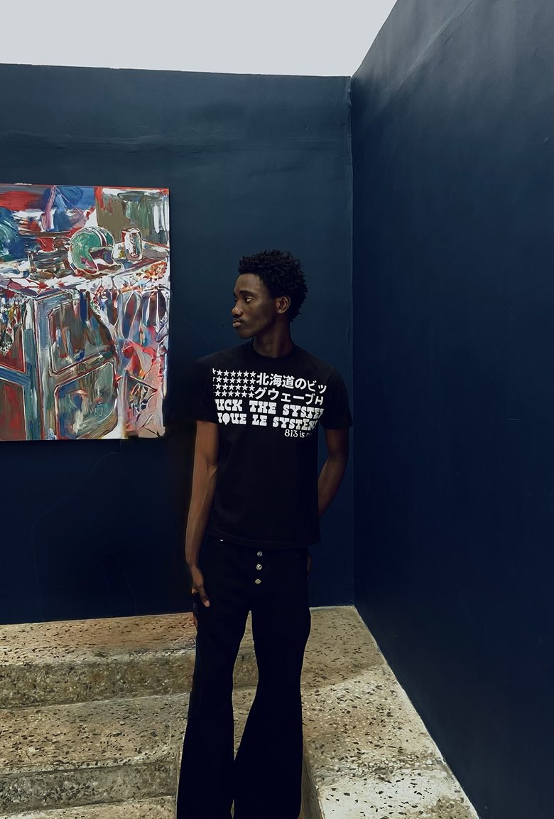 Kanann standing in a dark blue gallery corner beside a colourful painting