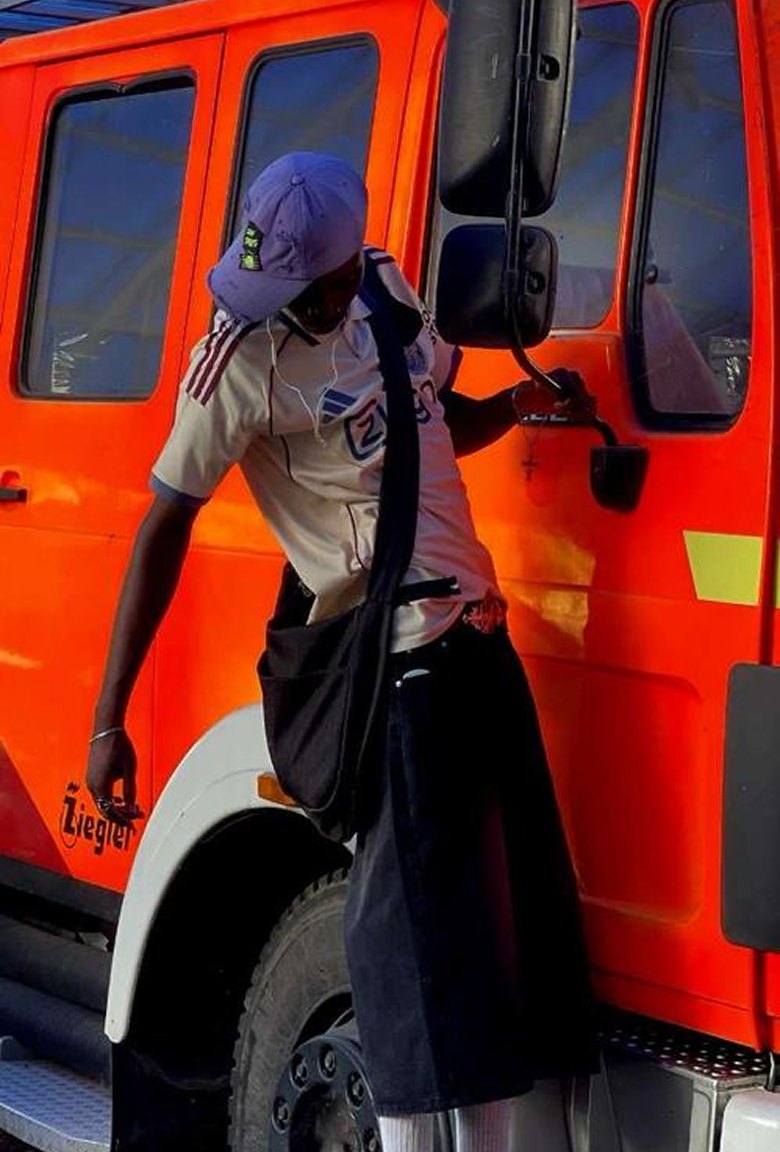 Kanann leaning against an orange fire truck in a purple cap