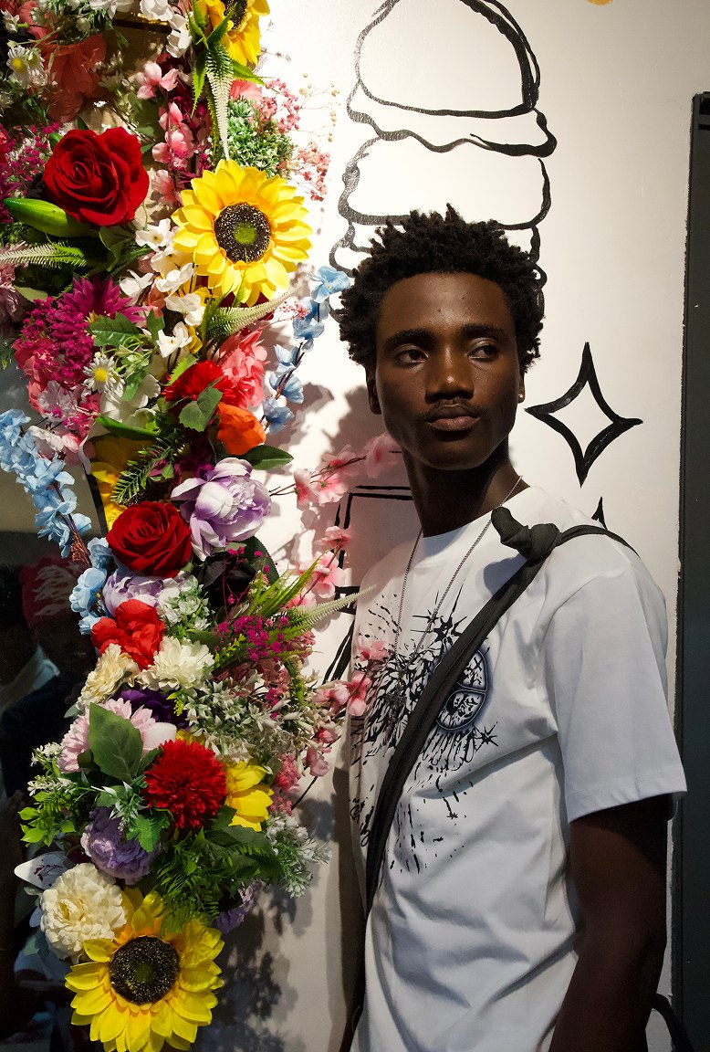 Kanann in a white tee standing beside a wall of flowers